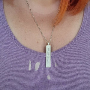 May include: A silver necklace with a rectangular pendant that reads "Hello Lady Vengeance".