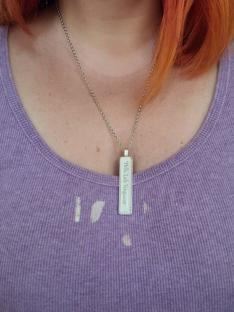 May include: A silver necklace with a rectangular pendant that reads "Hello Lady Vengeance".