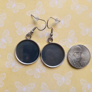 Pu&ograve; includere: Un paio di orecchini d'argento con cabochon rotondi, neri e dall'aspetto vetroso. Gli orecchini sono mostrati accanto a una moneta da 20 centesimi di euro per il confronto delle dimensioni.