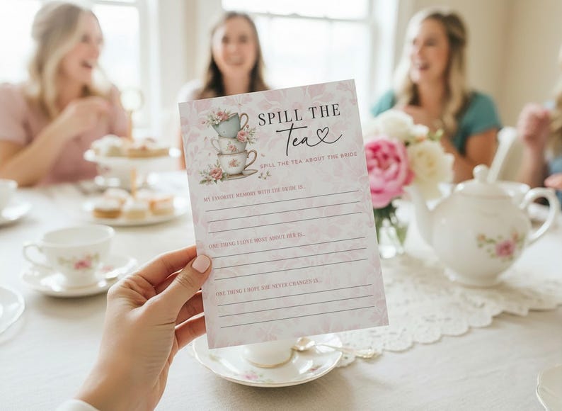 Op de afbeelding: Een roze en witte vrijgezellenfeest-spelkaart met de tekst "Spill the Tea" en een illustratie van een stapel theekopjes. De kaart heeft lijnen om op te schrijven, met een bloemenontwerp en een theekopje en theepot op de achtergrond.