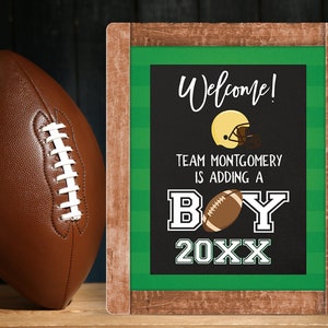 May include: A chalkboard sign with a green and white striped border announcing a baby boy. The sign reads "Welcome! Team Montgomery is adding a boy 20XX". A football helmet and football are illustrated on the sign.