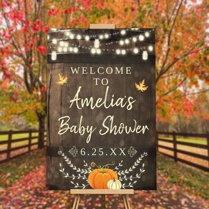 May include: Welcome to Amelia's Baby Shower sign with a rustic woodgrain background, string lights, fall leaves, and pumpkins. The date is 6.25.XXX.