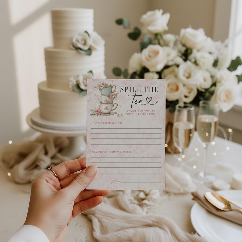 Op de afbeelding: Een hand houdt een roze en witte "Spill the Tea" advieskaart voor een bruidsfeest. De kaart toont gestapelde theekopjes en bloemmotieven. Een drielaagse taart en een boeket witte rozen staan op de achtergrond.