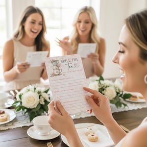 Op de afbeelding: Een roze en witte spelkaart met de tekst "Spill the Tea" en een illustratie van een theekopje. De kaart wordt door een persoon vastgehouden, met twee andere personen op de achtergrond. De spelkaart is voor een bruidsfeest.