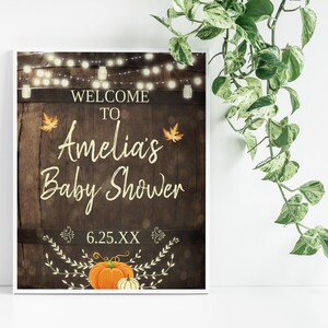 May include: A rustic wooden sign with string lights, leaves, and a pumpkin. The sign says "Welcome to Amelia's Baby Shower 6.25.XX".