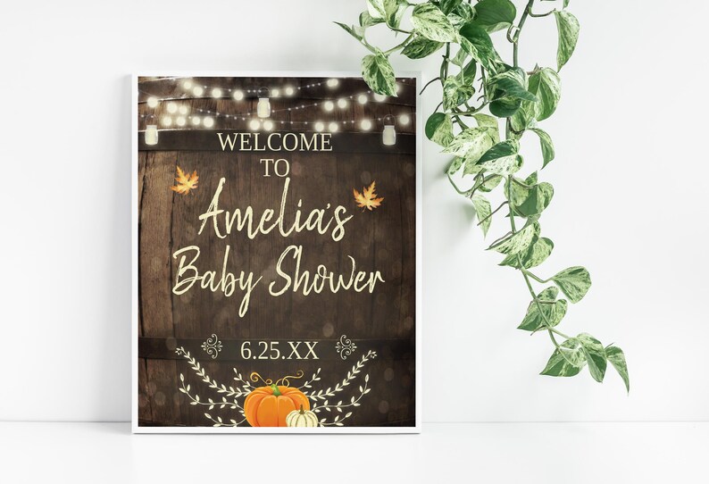 May include: A rustic wooden sign with string lights, leaves, and a pumpkin. The sign says "Welcome to Amelia's Baby Shower 6.25.XX".