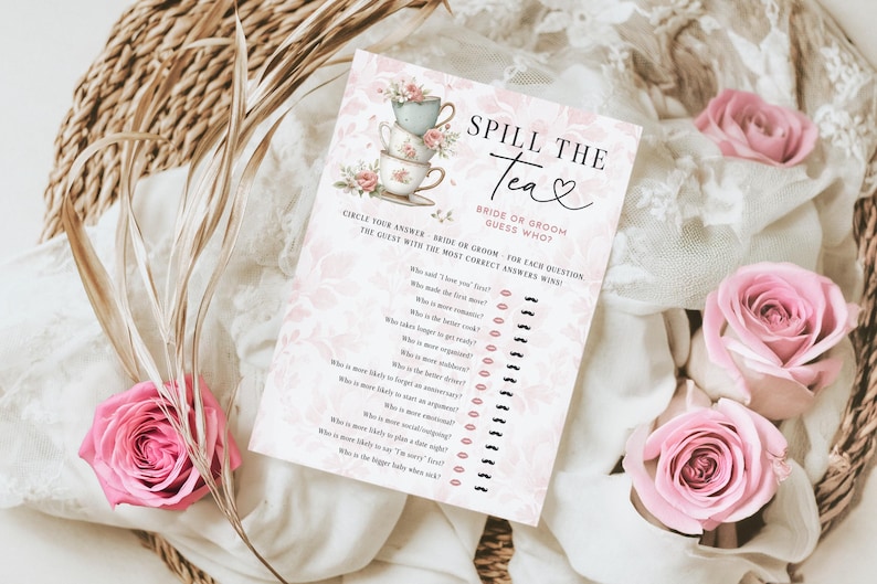 Op de afbeelding: Een roze en witte bruidsdouche-spelkaart met de tekst "Spill the Tea". De kaart heeft een stapel theekopjes en bloemaccenten. Roze rozen en gedroogde planten omringen de kaart.