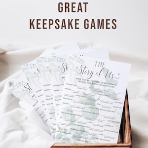 K&ouml;nnte beinhalten: Ein Stapel wei&szlig;er Spielkarten mit einem gr&uuml;nen Blumendesign und dem Text "The Story of Us". Die Karten befinden sich in einer Holzkiste. Der Text "Great Keepsake Games" steht oben.