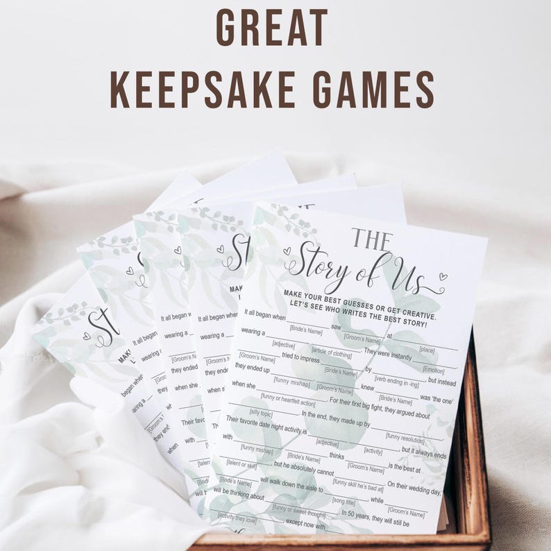 K&ouml;nnte beinhalten: Ein Stapel wei&szlig;er Spielkarten mit einem gr&uuml;nen Blumendesign und dem Text "The Story of Us". Die Karten befinden sich in einer Holzkiste. Der Text "Great Keepsake Games" steht oben.