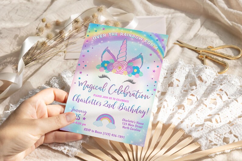 May include: A rainbow-themed invitation for a child's 2nd birthday party. The invitation features a unicorn with a flower crown and the text "Over the Rainbow for a Magical Celebration. Please join us to celebrate Charlotte's 2nd Birthday!"