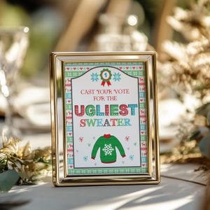 May include: A gold-framed sign with a red, green, and white patterned border. The sign says "Cast your vote for the Ugliest Sweater" and features a cartoon green sweater with a snowflake design.