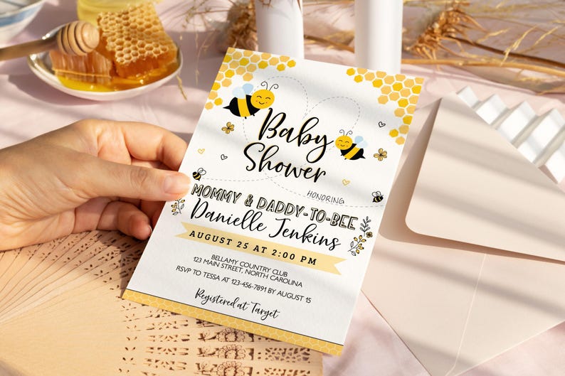 Może przedstawiać: Białe zaproszenie na baby shower z ż&oacute;łto-czarnym wzorem plastra miodu. Zaproszenie zawiera napis "Baby Shower" i "Mommy & Daddy-to-Bee Danielle Jenkins". Data i godzina imprezy to 25 sierpnia o 14:00. Miejscem imprezy jest Bellamy Country Club, 123 Main Street, Karolina P&oacute;łnocna. Informacje RSVP należy przekazać Tessie pod numer 123-456-7891 do 15 sierpnia. Zaproszenie zawiera r&oacute;wnież napis "Registered at Target".