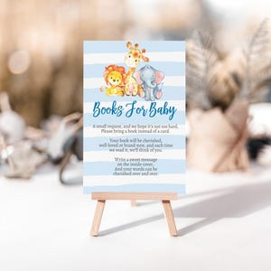 May include: A baby shower sign with a blue and white striped background. The sign features illustrations of a lion, giraffe, and elephant. Text on the sign reads "Books For Baby" and requests guests to bring a book instead of a card.