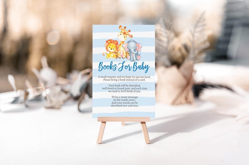 May include: A baby shower sign with a blue and white striped background. The sign features illustrations of a lion, giraffe, and elephant. Text on the sign reads "Books For Baby" and requests guests to bring a book instead of a card.