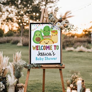 May include: Welcome to Jessica's Baby Shower sign with a colorful rainbow font. The sign features a cartoon avocado, cactus, taco, and burrito with smiling faces.