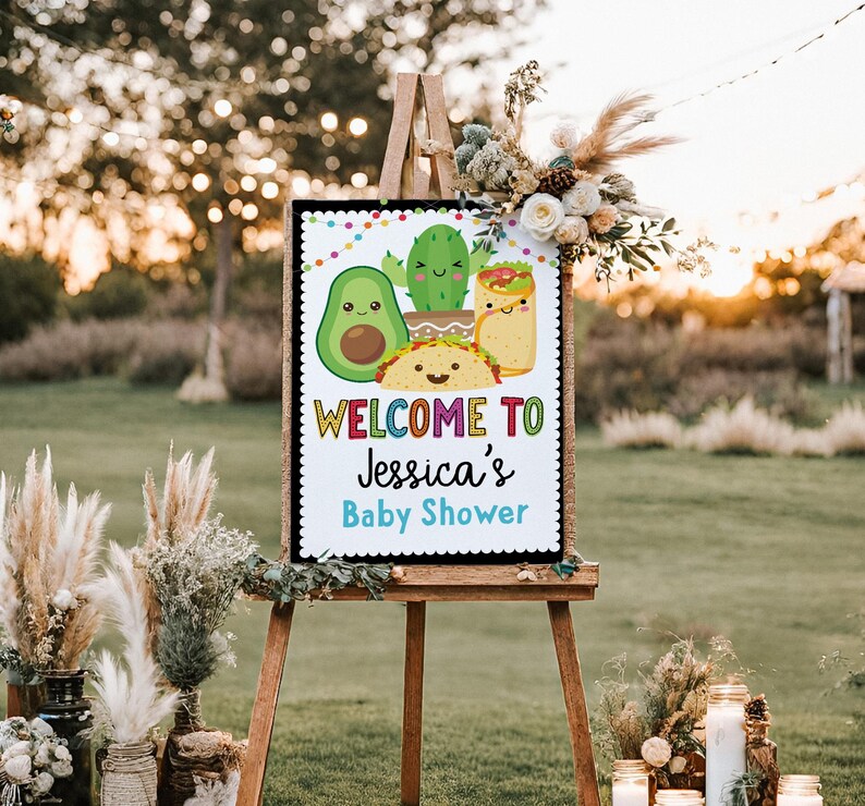 May include: Welcome to Jessica's Baby Shower sign with a colorful rainbow font. The sign features a cartoon avocado, cactus, taco, and burrito with smiling faces.