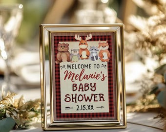 Puede incluir: Un cartel con marco dorado y fondo de cuadros rojos y negros. El cartel presenta un mensaje de bienvenida para la baby shower de Melanie, junto con una fecha del 2.15.XX. El cartel también incluye una linda ilustración de animales del bosque, incluyendo un ciervo, un oso, un mapache y un búho.