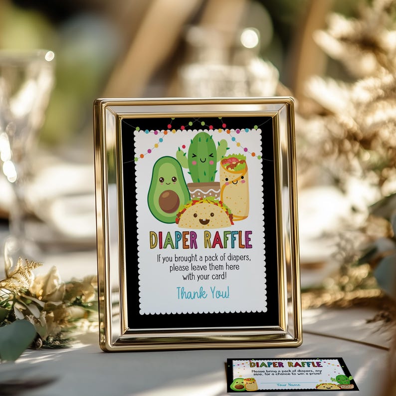 May include: A gold-framed sign with a black background and colorful text that reads "Diaper Raffle". The sign features a cartoon avocado, cactus, and taco with smiling faces. The text below the image reads "If you brought a pack of diapers, please leave them here with your card! Thank You."