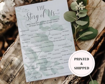 Puede incluir: Tarjeta de juego para rellenar, "The Story of Us", con un diseño floral. La tarjeta tiene indicaciones para que los invitados las completen, con "Printed & Shipped" en un círculo en la parte inferior derecha. Sobre una superficie de madera.
