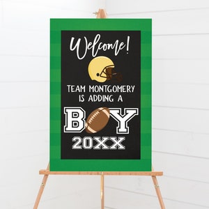 May include: A green and black chalkboard sign with white text announcing a baby boy. The sign says "Welcome! Team Montgomery is adding a BOY 20XX" with a football and a football helmet graphic.