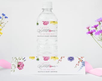 Peut inclure: Une bouteille d'eau blanche avec une étiquette à motif floral qui dit "A Little Wildflower Is On The Way Olivia's Baby Shower". L'étiquette présente des fleurs roses, jaunes et vertes. Il y a une étiquette assortie avec le même design sur un fond blanc.