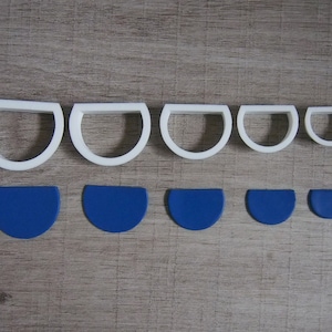 May include: Set of six white plastic cookie cutters in various sizes shaped like half circles. The cutters are arranged in a row from largest to smallest. Below the cutters are six blue fondant pieces, also in various sizes, shaped like half circles.