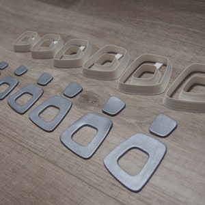 Puede incluir: Un conjunto de 10 anillos de metal plateado y blanco, dispuestos en dos filas. Los anillos son de diferentes tamaños y están anidados unos dentro de otros.