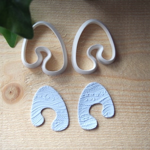 May include: Two white plastic cookie cutters shaped like an arch with a wavy design inside. Two light blue fondant shapes with the same design, but with a textured pattern.