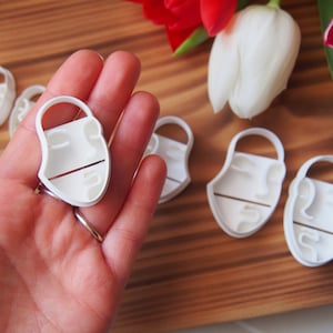 May include: A set of five white plastic cookie cutters shaped like a face. The cutters are on a wooden surface.