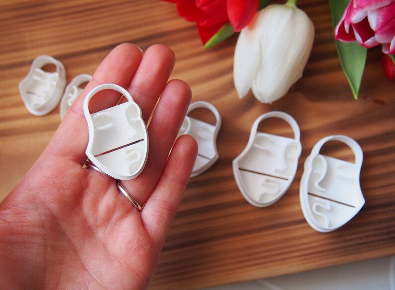 May include: A set of five white plastic cookie cutters shaped like a face. The cutters are on a wooden surface.