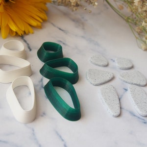 May include: A set of polymer clay cutters featuring a variety of shapes. The cutters are in white and green, and include oval, teardrop, and leaf shapes.