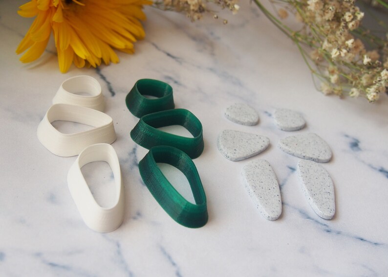 May include: A set of polymer clay cutters featuring a variety of shapes. The cutters are in white and green, and include oval, teardrop, and leaf shapes.