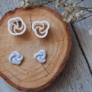 May include: Two white plastic molds shaped like a rose and two gray polymer clay roses on a wooden surface.