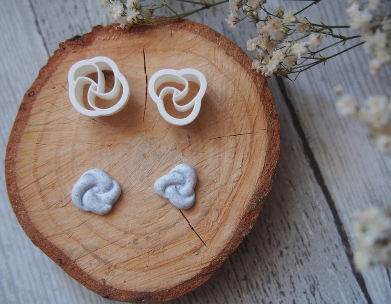 May include: Two white plastic molds shaped like a rose and two gray polymer clay roses on a wooden surface.