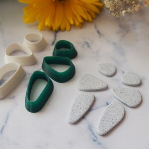 May include: A set of white and green polymer clay earring moulds. The moulds are shaped like teardrops and ovals. There are also six white speckled polymer clay earrings.