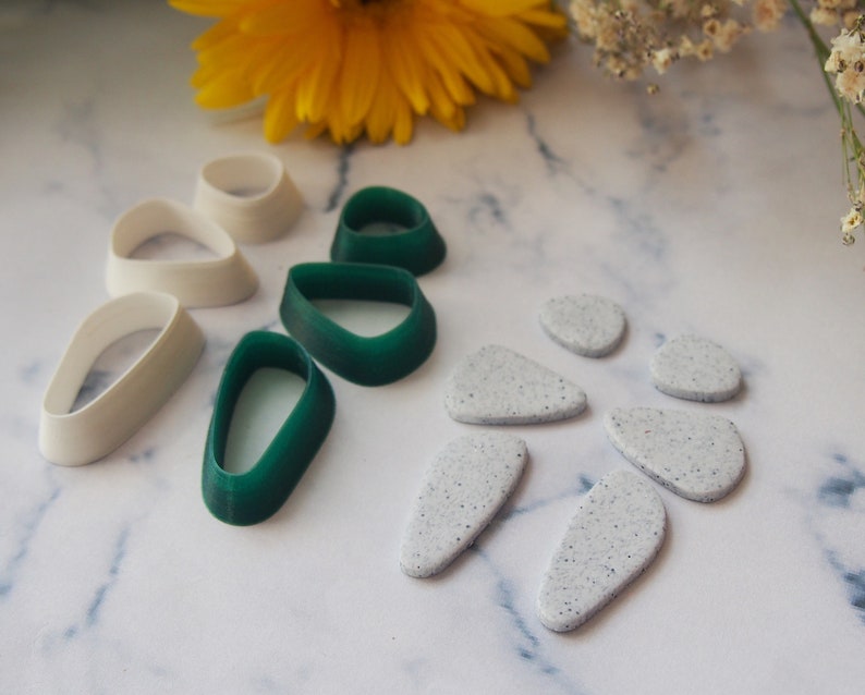 May include: A set of white and green polymer clay earring moulds. The moulds are shaped like teardrops and ovals. There are also six white speckled polymer clay earrings.
