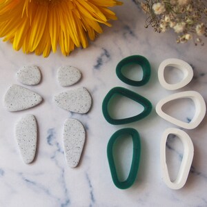 May include: A set of polymer clay earring shapes in white and green. The set includes six shapes: two teardrop shapes, two oval shapes, and two round shapes. The white shapes are speckled with white glitter.