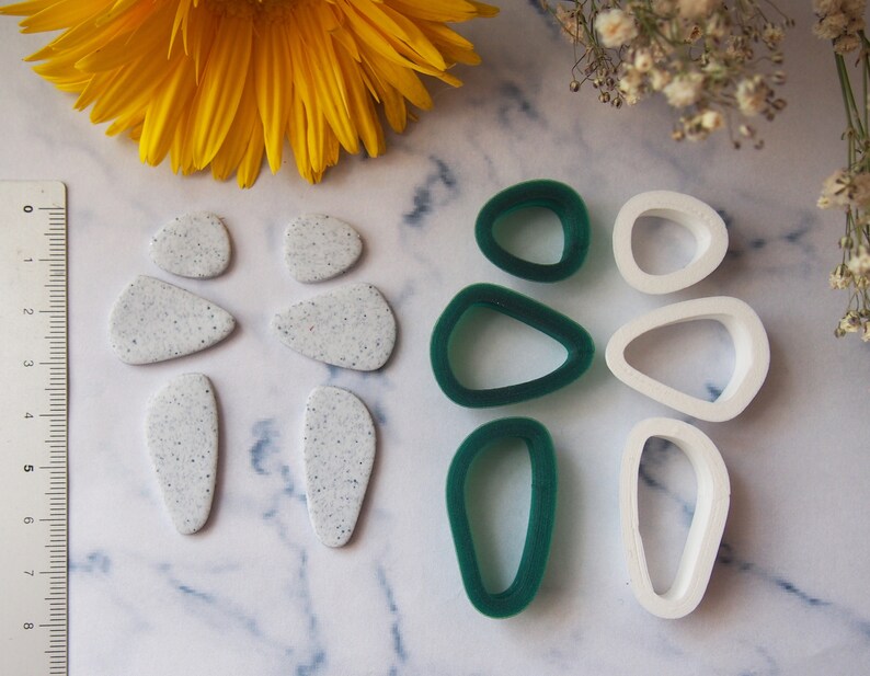 May include: A set of polymer clay earring shapes in white and green. The set includes six shapes: two teardrop shapes, two oval shapes, and two round shapes. The white shapes are speckled with white glitter.