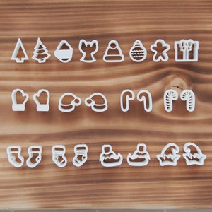 Könnte beinhalten: Ein Set mit 18 weißen Weihnachts-Ausstechformen aus Kunststoff, darunter Formen wie ein Weihnachtsbaum, ein Strumpf, eine Mütze, ein Zuckerstange und eine Weihnachtsmannmütze.
