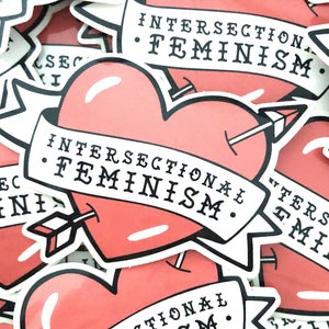 May include: A close-up of several stickers with a heart design and the text "INTERSECTIONAL FEMINISM." The stickers are pink and white with black lettering.