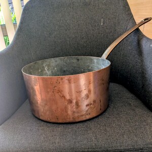 Puede incluir: Una taza de cerámica blanca con un asa negra y el texto "But First, Coffee" en negrita negra. La taza se encuentra sobre un fondo borroso, sugiriendo un ambiente acogedor.