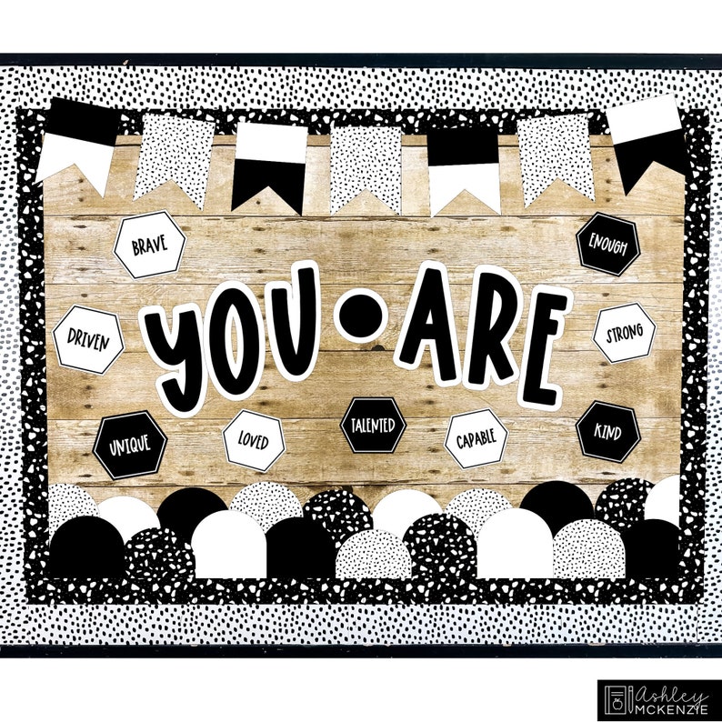 May include: Black and white classroom bulletin board with the words "YOU ARE" in large, bold letters. The board is decorated with black and white polka dot patterned borders, pennants, and half circles. There are also hexagonal shapes with positive affirmations such as "Brave", "Driven", "Unique", "Loved", "Talented", "Capable", "Enough", "Strong", "Kind".