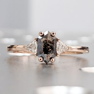 May include: A rose gold engagement ring with a black octagon-shaped diamond and two smaller diamonds on either side.