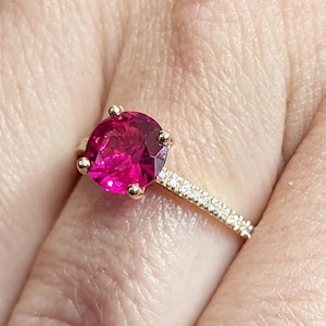 May include: A gold ring featuring a large, round, pink gemstone and a band of small, white gemstones.