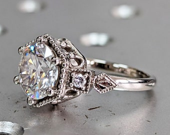 May include: A silver engagement ring with a large, round, clear center stone and smaller accent stones. The ring has a delicate, vintage-inspired design.