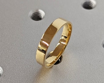 May include: A simple gold band ring on a gray textured surface with evenly spaced holes.