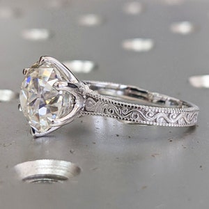 May include: A silver engagement ring with a large, round, clear diamond and an intricate, engraved band.