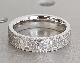 May include: A silver wedding band with an intricate engraved design of swirling leaves.