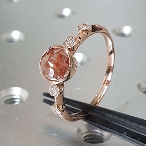 May include: A rose gold ring featuring a round, brown and clear gemstone, surrounded by smaller clear gemstones.