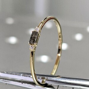 May include: A delicate gold band ring with a small, rectangular, grey diamond and two smaller clear diamonds.